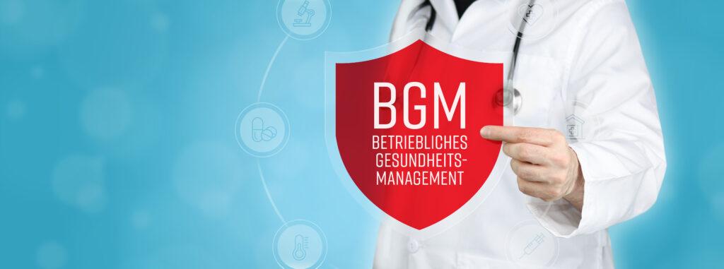 Arzt zeigt ein Schutzschild mit der Aufschrift "BGM – Betriebliches Gesundheitsmanagement" als Symbol für Gesundheitsförderung im Unternehmen.